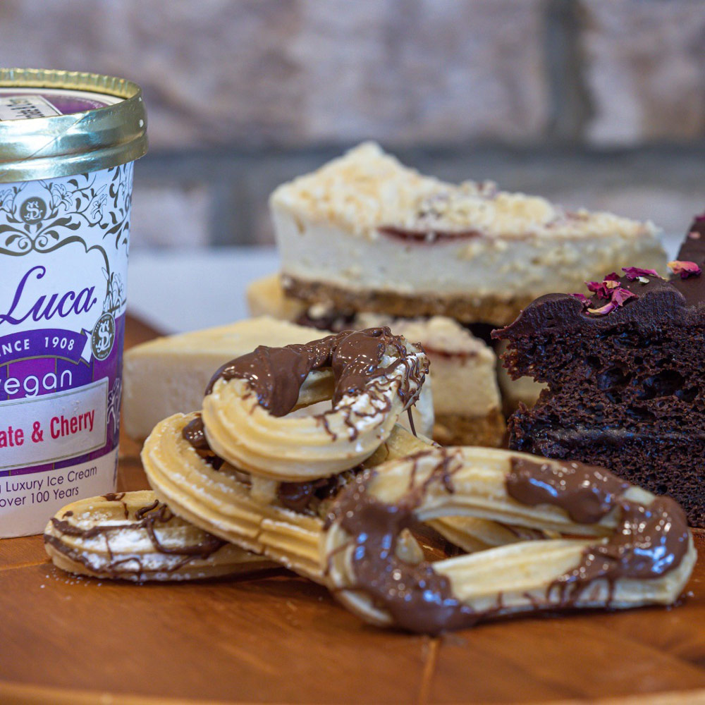 Collection of benes desserts, including several churros, slices of cheesecake, and chocolate cake. 